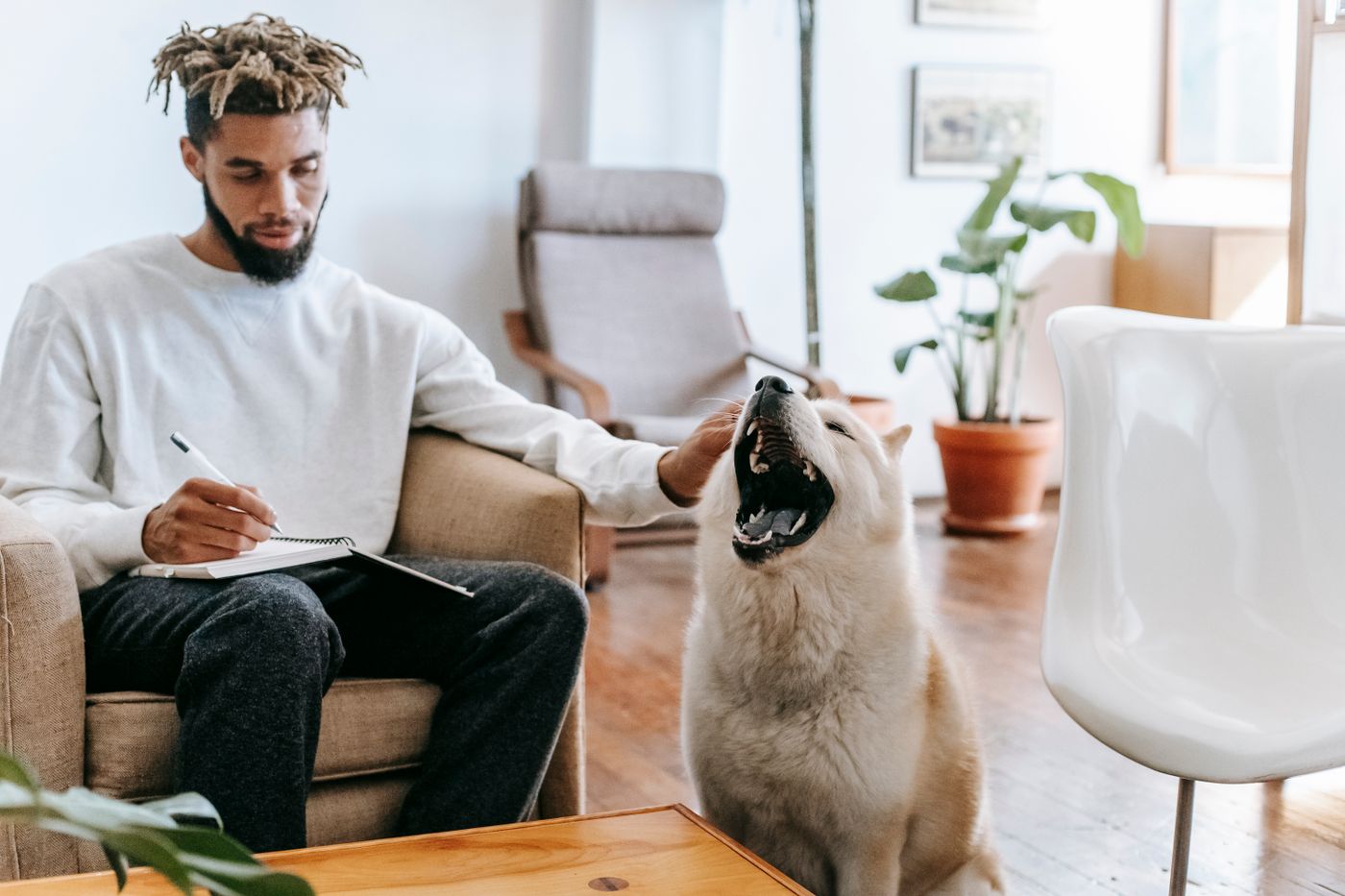 A person writing in a notebook beside a dog at home.