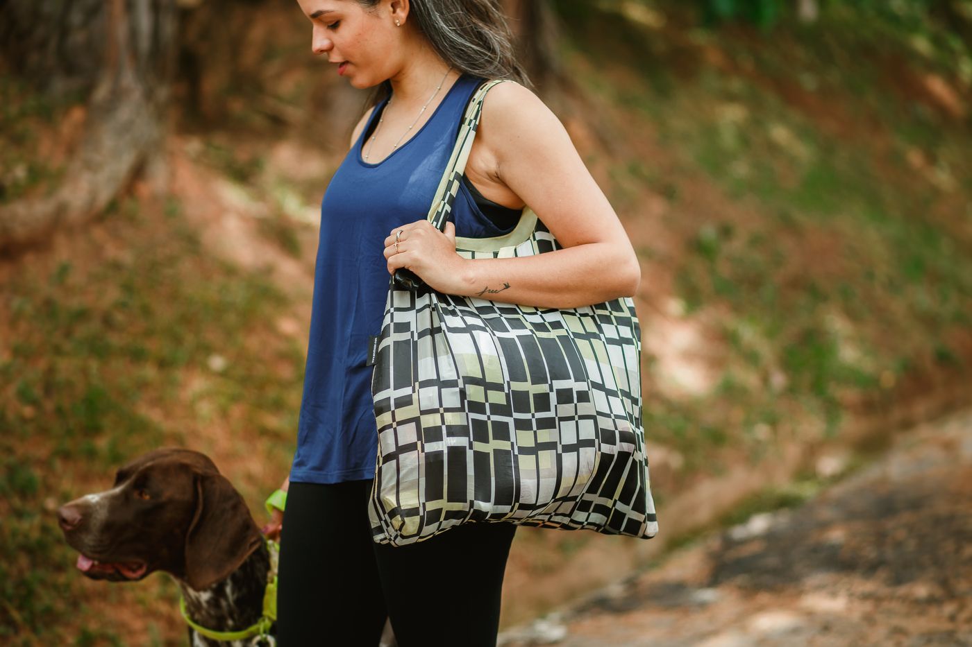 A person carrying a roomy bag while walking a dog.